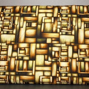 May include: Geometric patterned fabric in shades of brown, green, and cream. The design features a repeating block pattern with a woven or basket-like appearance. The fabric is folded, showing the pattern's repeating nature.