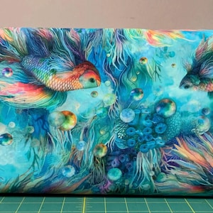 May include: Fabric with a vibrant underwater scene featuring colorful betta fish. The fish have flowing fins in shades of orange, yellow, blue, and green. Bubbles and aquatic plants add to the aquatic theme, set against a turquoise background.