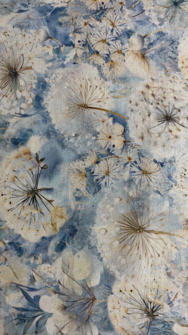 以下が含まれることがあります： 花柄の生地のクローズアップ。白い羽のような種子と繊細な花が、水色とベージュの背景にデザインされています。生地はテクスチャード加工されています。