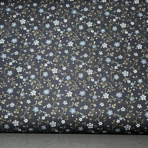 May include: Dark navy fabric with a repeating floral pattern. The design features small white and light blue flowers with brown stems and leaves. The fabric is rolled up, showing the pattern's detail.