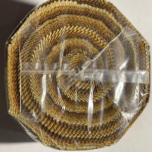 May include: A roll of fabric with a repeating pattern of brown and tan feather-like shapes. The fabric is tightly rolled and wrapped in clear plastic, secured with clear tape. The overall shape is octagonal.