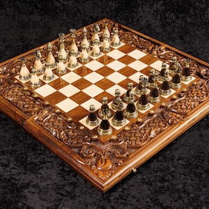 May include: A detailed, wooden chess set with intricately carved borders. The chessboard features a light and dark square pattern, with gold and silver chess pieces arranged for play. The set is displayed on a dark, textured surface.