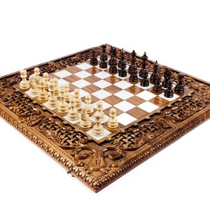 May include: A wooden chess set with intricately carved detailing around the board's perimeter. The chess pieces are arranged on a checkered board, with light and dark pieces ready for play. The set is displayed on a white background.