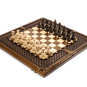 May include: A wooden chess set with a dark brown, intricately carved border. The chessboard features a light and dark square pattern, with chess pieces arranged for play. The pieces are in black and cream colors.