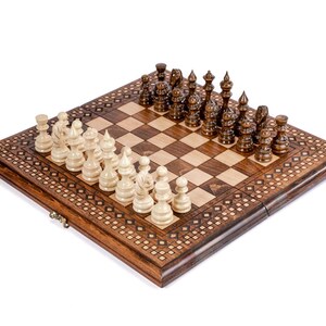 May include: A wooden chess set with a decorative border. The chess pieces are light and dark brown. The board is set up, ready for a game. The board is made of wood and has a checkered pattern.