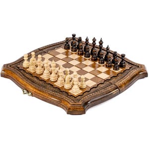 Op de afbeelding: Een houten schaakspel met een decoratieve rand. Het schaakbord is vierkant met afwisselend lichte en donkere vakken. De schaakstukken zijn zwart en licht van kleur. De set staat op een witte achtergrond.