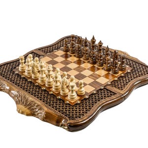 May include: A wooden chess set with a decorative border. The chessboard is made of light and dark wood squares, with chess pieces set up for play. The border has a woven pattern and ornate detailing.