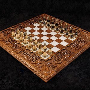 May include: A wooden chess set with intricately carved borders. The chessboard features a brown and white checkered pattern. Chess pieces are gold and black. The set is displayed on a dark background.