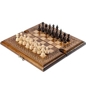 May include: A wooden chess set with a decorative border. The chessboard is open, displaying the light and dark squares. The chess pieces are arranged on the board, with black and white pieces facing each other. The set is on a white background.