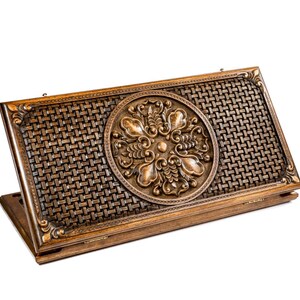 May include: A wooden backgammon board with a detailed, woven pattern and a central, circular, floral design. The board is a warm brown color and appears to be made of high-quality wood. The board is open, revealing the playing surface.