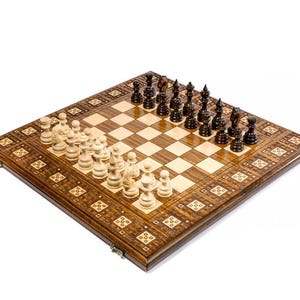 May include: A wooden chess set with a decorative border. The chessboard is brown and beige with black and white chess pieces arranged for play. The set is on a white background.