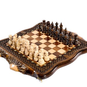 May include: A wooden chess set with a dark brown, intricately carved border. The chessboard features a light and dark brown checkered pattern. Chess pieces are in place, with light and dark brown pieces ready to play.