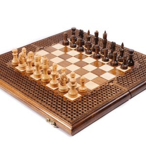 May include: A wooden chess set with light and dark brown squares and intricately carved borders. The chess pieces are arranged on the board, with light-colored pieces on one side and dark-colored pieces on the other.