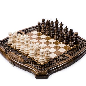 May include: A wooden chess set with a dark brown, intricately carved border. The chessboard features a light and dark square pattern, with light-colored and dark-colored chess pieces arranged on the board. The set is displayed on a white background.