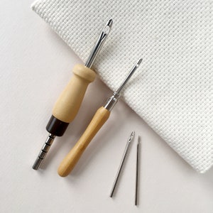 May include: A set of four embroidery tools, including two wooden handled needle threaders and two metal needles. The tools are on a white background.