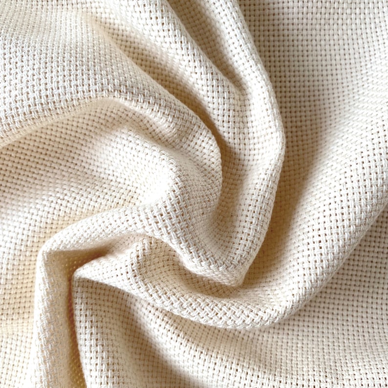 May include: Close-up of a cream-colored fabric with a woven texture. The fabric is folded and draped, creating soft folds and curves.