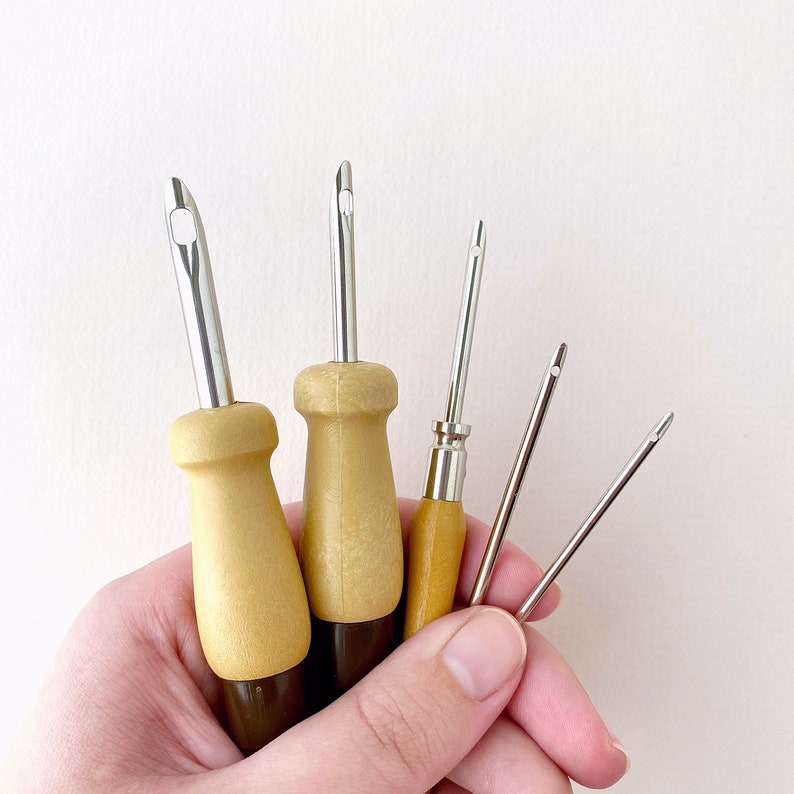May include: Five different sized crochet hooks with wooden handles. The hooks are held in a hand.