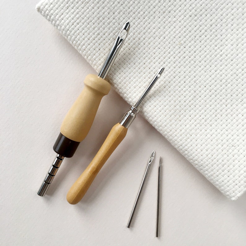 May include: A set of four embroidery tools, including two wooden handled needle threaders and two metal needles. The tools are on a white background.