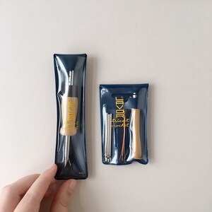 May include: Two sets of crochet tools in clear plastic pouches with blue trim. The pouches have the text "Trick Crochet" and a logo. One set includes a wooden crochet hook and the other set includes a wooden handle with multiple crochet hooks.