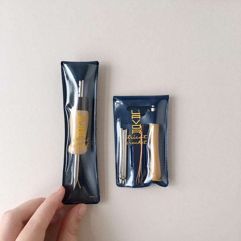 May include: Two sets of crochet tools in clear plastic pouches with blue trim. The pouches have the text "Trick Crochet" and a logo. One set includes a wooden crochet hook and the other set includes a wooden handle with multiple crochet hooks.
