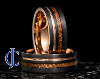 May include: Two black tungsten carbide rings with a rose gold inlay and a wood grain pattern. The rings are stacked on top of each other.