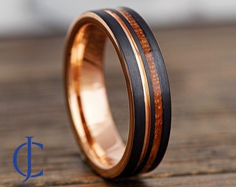 May include: A black tungsten carbide ring with a rose gold inlay and a wood inlay. The ring has a brushed finish.