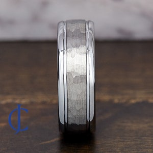 Puede incluir: Un anillo de carburo de tungsteno plateado con acabado martillado y dos bordes biselados pulidos.