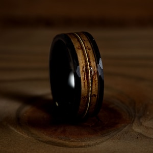 May include: A black and brown ring with a gold inlay. The ring is made of wood and metal.