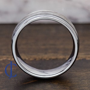 Puede incluir: Un anillo de carburo de tungsteno plateado con un borde biselado y un acabado cepillado.