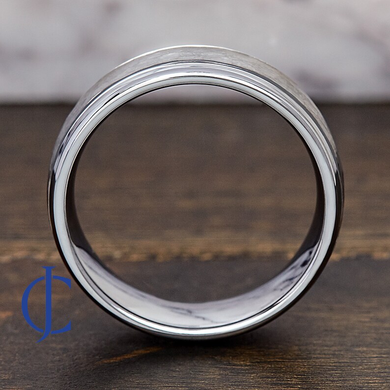 Puede incluir: Un anillo de carburo de tungsteno plateado con un borde biselado y un acabado cepillado.