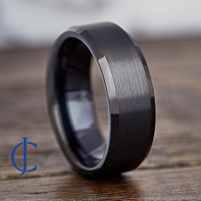 May include: A black tungsten carbide ring with a beveled edge and a brushed finish.