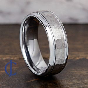 Puede incluir: Un anillo de carburo de tungsteno plateado con acabado martillado y borde biselado pulido.