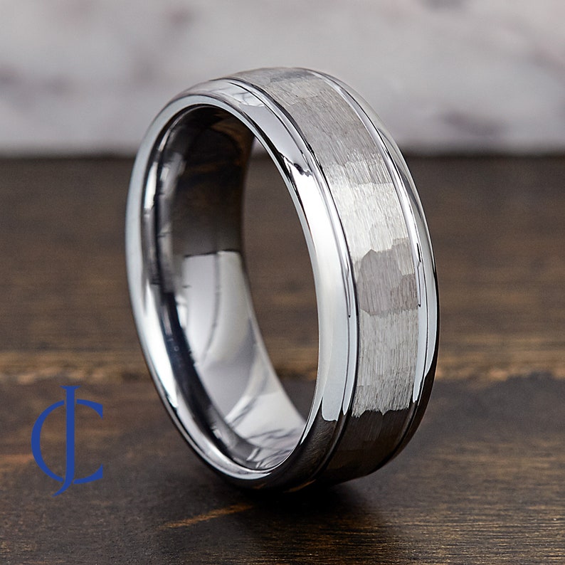 Puede incluir: Un anillo de carburo de tungsteno plateado con acabado martillado y borde biselado pulido.