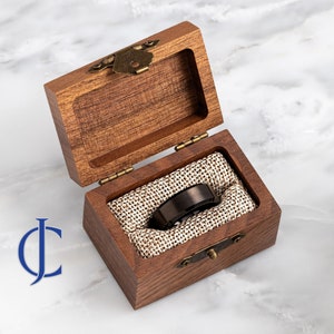 May include: A black tungsten carbide ring with a beveled edge, displayed in a wooden box with a fabric lining.