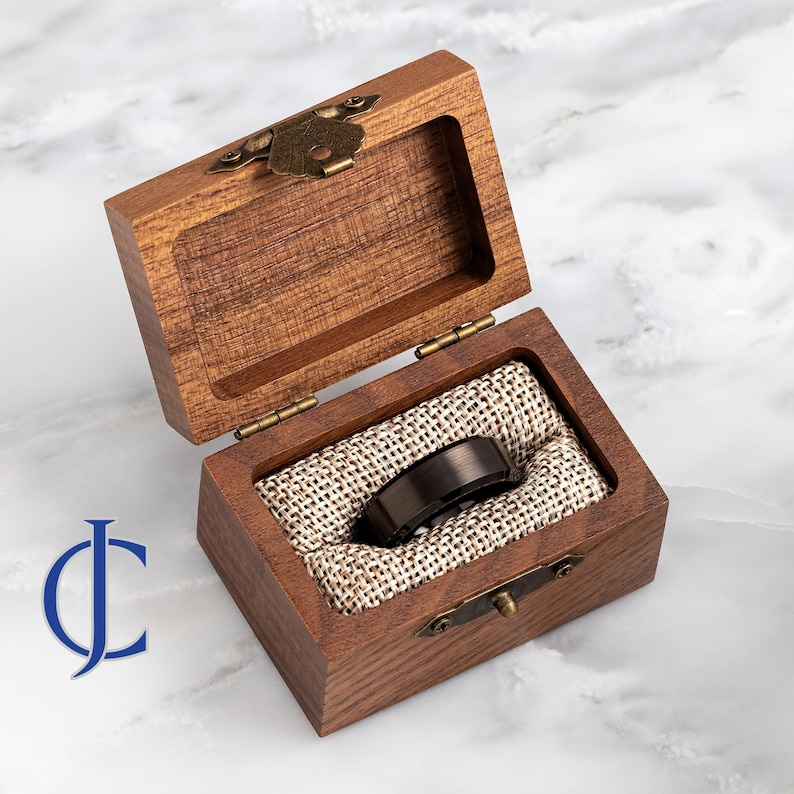 May include: A black tungsten carbide ring with a beveled edge, displayed in a wooden box with a fabric lining.
