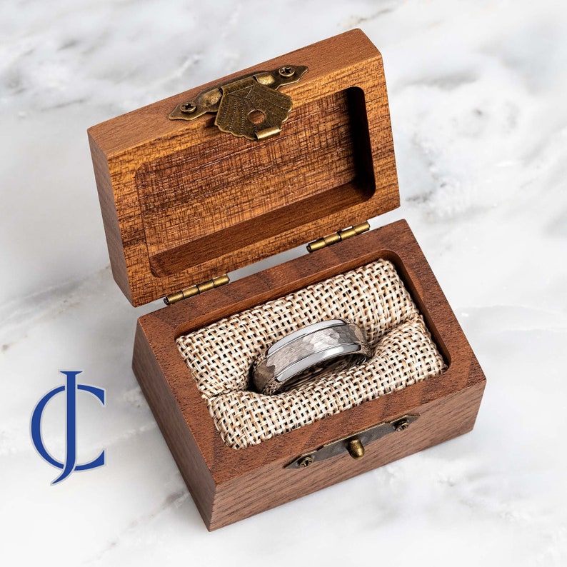 Puede incluir: Un anillo de metal martillado plateado y blanco en una caja de madera con tapa abatible y cierre de lat&oacute;n.