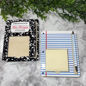 May include: Two wooden notepads with a pen attached. The notepad on the left has a black and white composition book design with the text "Composition Book" and "100 Sheets 200 Pages". The notepad on the right has a blue and white lined paper design.