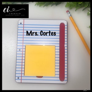 May include: A white notepad with blue lines and a red pencil holder. The notepad has a yellow sticky note and the text "Mrs. Cortes" printed on it.