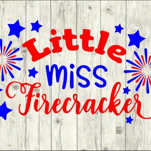 May include: Red and blue text on a white wood background reads "Little miss firecracker". The text is surrounded by red and blue fireworks and stars.