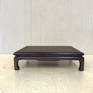 May include: A dark brown, rectangular wooden display stand with a raised, square top and curved legs. The stand is designed to elevate and showcase objects. The background features a striped pattern.