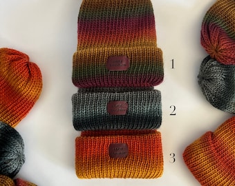 May include: Three knitted hats in different color combinations of orange, red, green, and black. The hats are stacked on top of each other. Each hat has a small leather tag with the text "Knit &  Co."