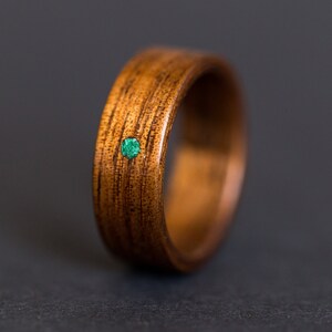 May include: A wooden ring with a green gemstone inlay. The ring is made of dark brown wood with a natural grain pattern.