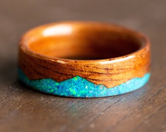 May include: A wooden ring with a blue and green opal inlay. The ring is made of dark wood and has a smooth finish.