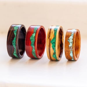 Può includere: Quattro anelli in legno con intarsi di pietre preziose. Gli anelli variano di colore, tra cui marrone scuro, rosso, marrone chiaro e una tonalità di legno più chiara. Ogni anello presenta una fascia di pietre verdi o turchesi.