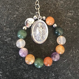 Puede incluir: Un llavero de plata con un dije de San Patricio y un brazalete de cuentas verdes, naranjas y moradas.