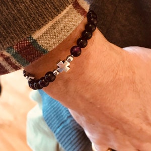 May include: A black beaded bracelet with a silver cross charm. The bracelet is made of small, round beads and has a simple, elegant design.