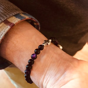 May include: A black beaded bracelet with a silver cross charm. The beads have a purple iridescent sheen.