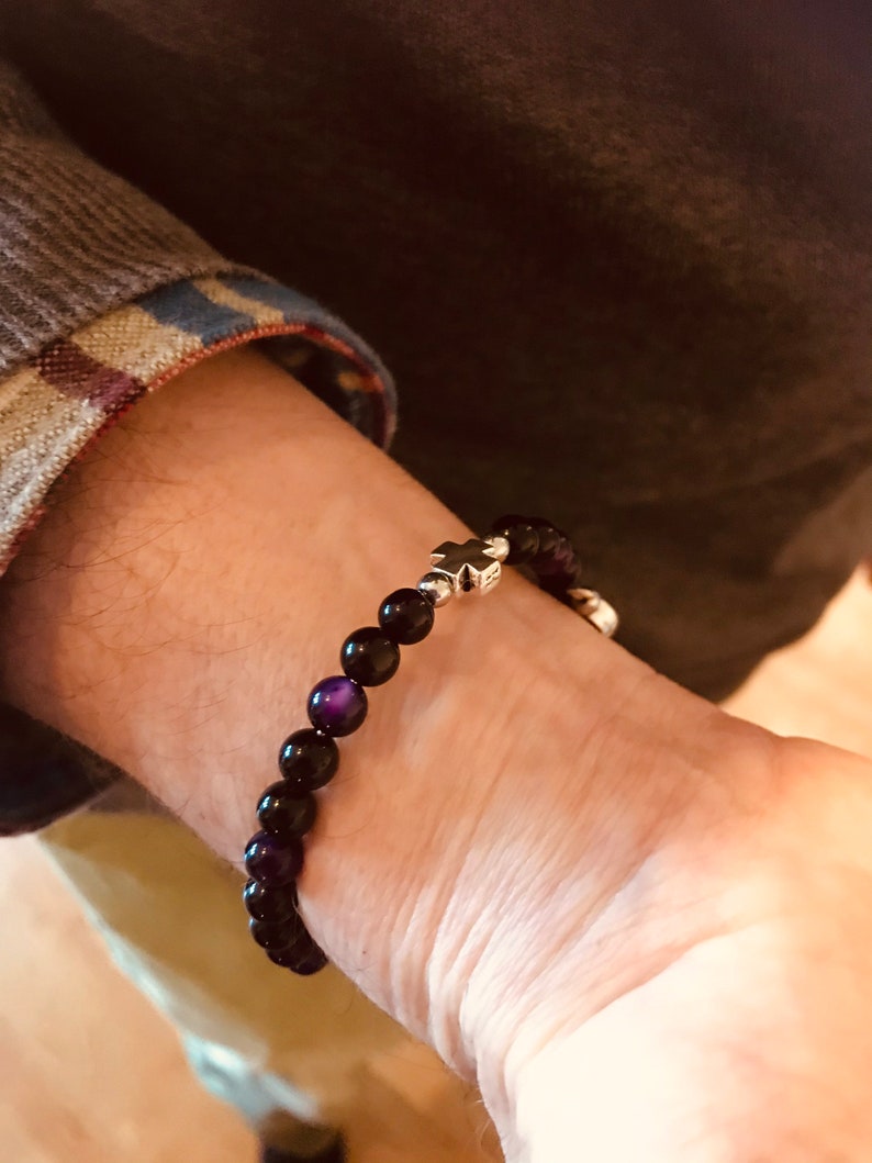 May include: A black beaded bracelet with a silver cross charm. The beads have a purple iridescent sheen.