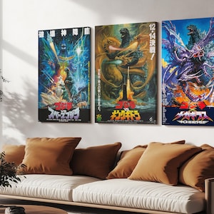 May include: Three framed movie posters featuring Godzilla and other monsters. The posters have vibrant colors and Japanese text. The posters are hanging above a white couch with brown pillows. The posters are a decorative element in a living room.