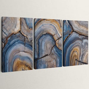May include: A three-panel wall art set featuring a high-resolution print of a cross-section of blue and gold agate stone. The design displays concentric rings, organic curves, and dark fissures, creating a continuous geological pattern across panels.